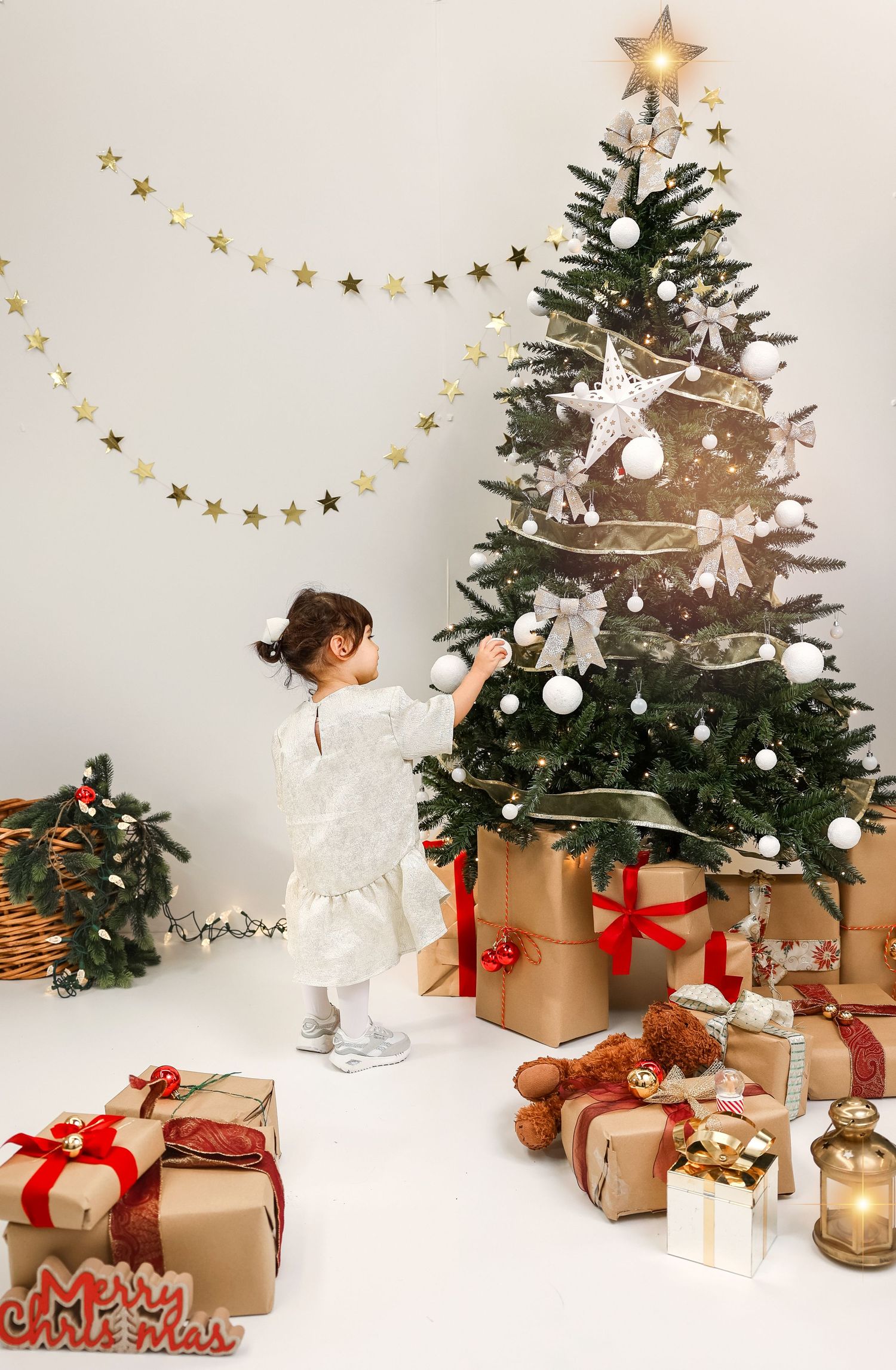 Elegant Christmas scene with decorated evergreen tree, wrapped presents in kraft paper, and golden star garland against white wall.