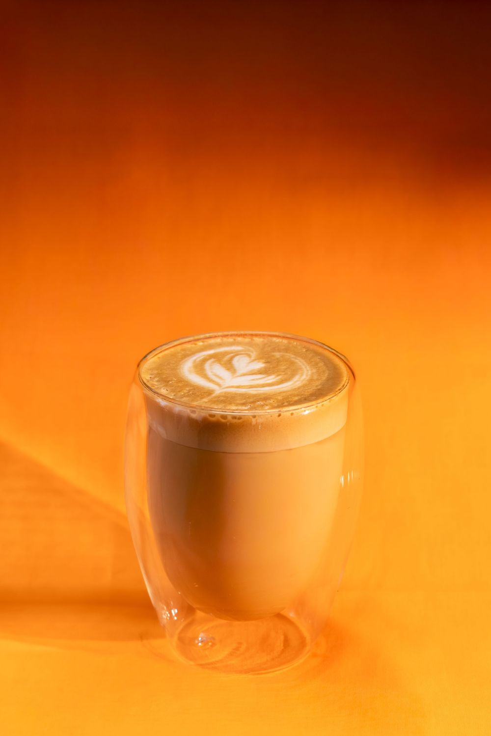 A sequence of coffee cups with latte art shown against a warm orange background creating an artistic gradient effect.