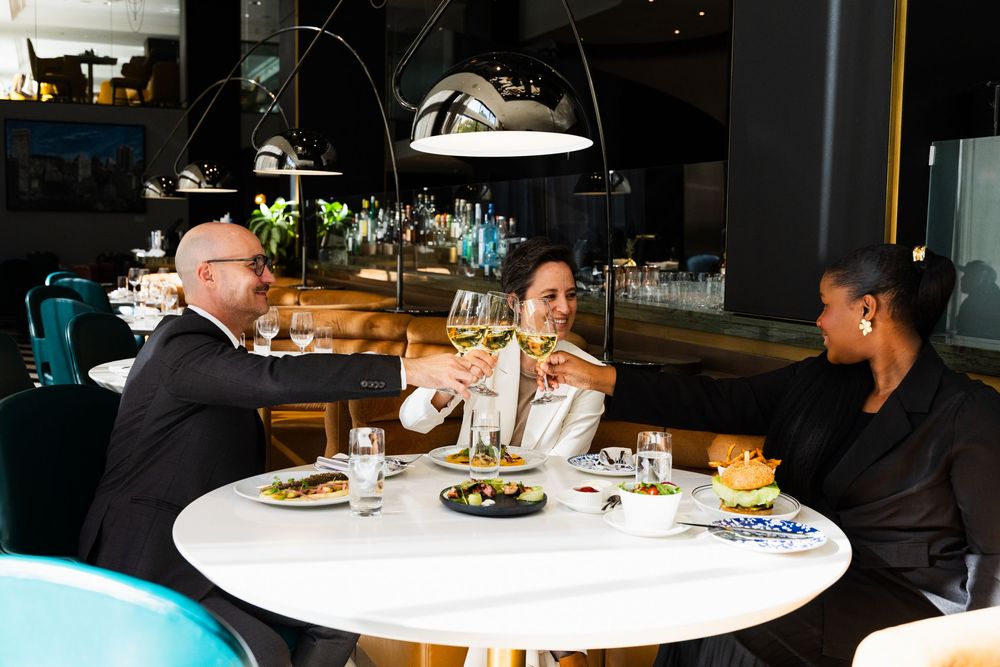 A group of diners enjoy a meal at a modern restaurant with white round tables and contemporary decor.