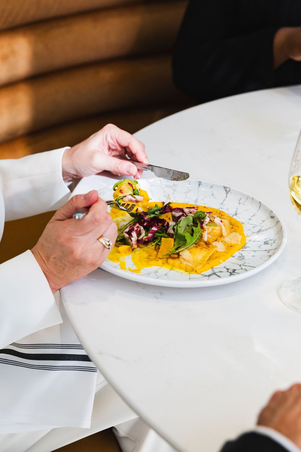 Close-up view of hands serving elegant plated yellow ravioli pasta garnished with fresh herbs on white dishes.