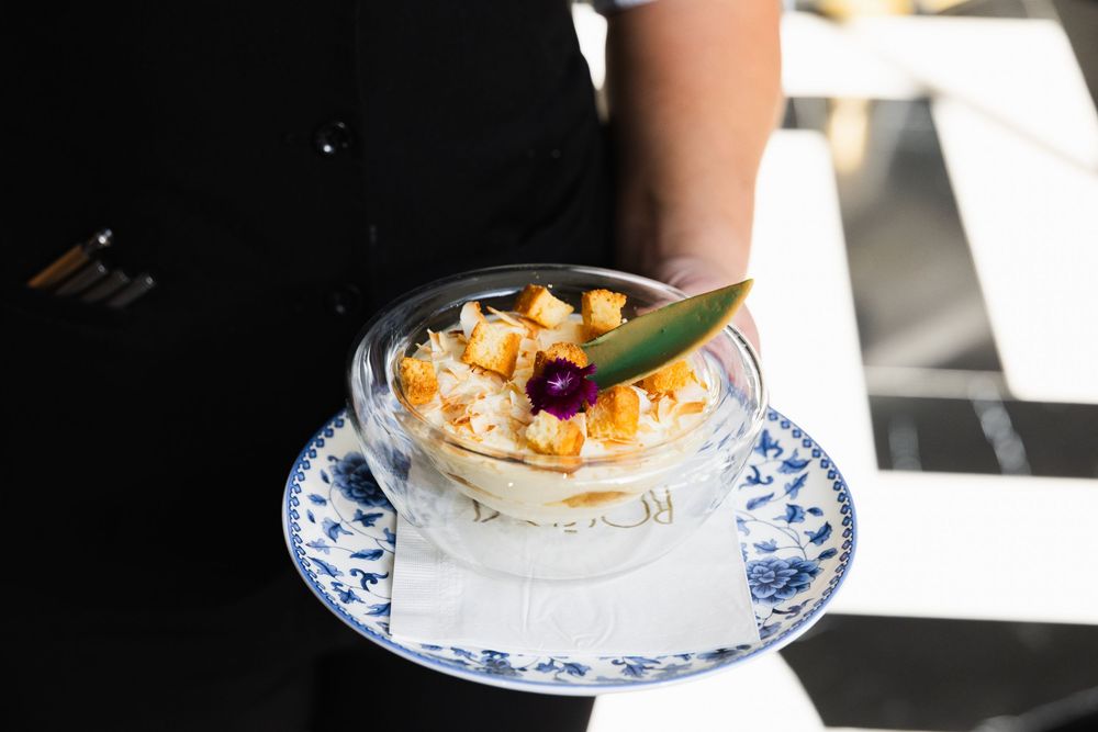 A bowl of creamy risotto garnished with shrimp and fresh herbs is being served on a blue and white patterned plate.