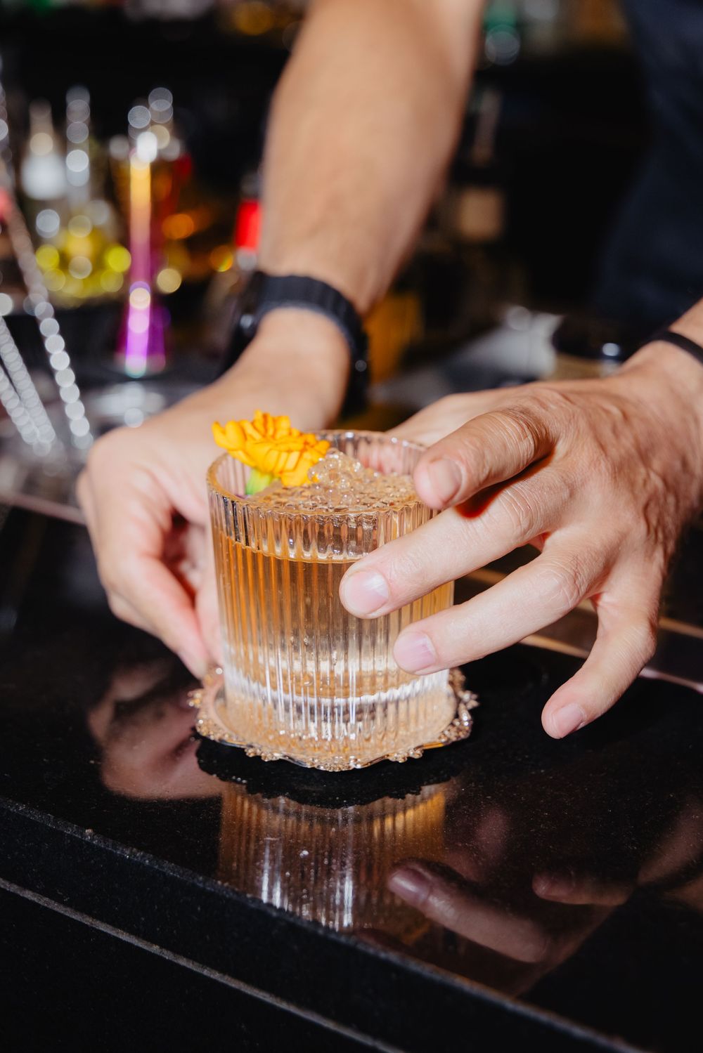 Hands placing a chocolate mousse dessert with orange garnish on a dark surface in a dimly lit restaurant setting.