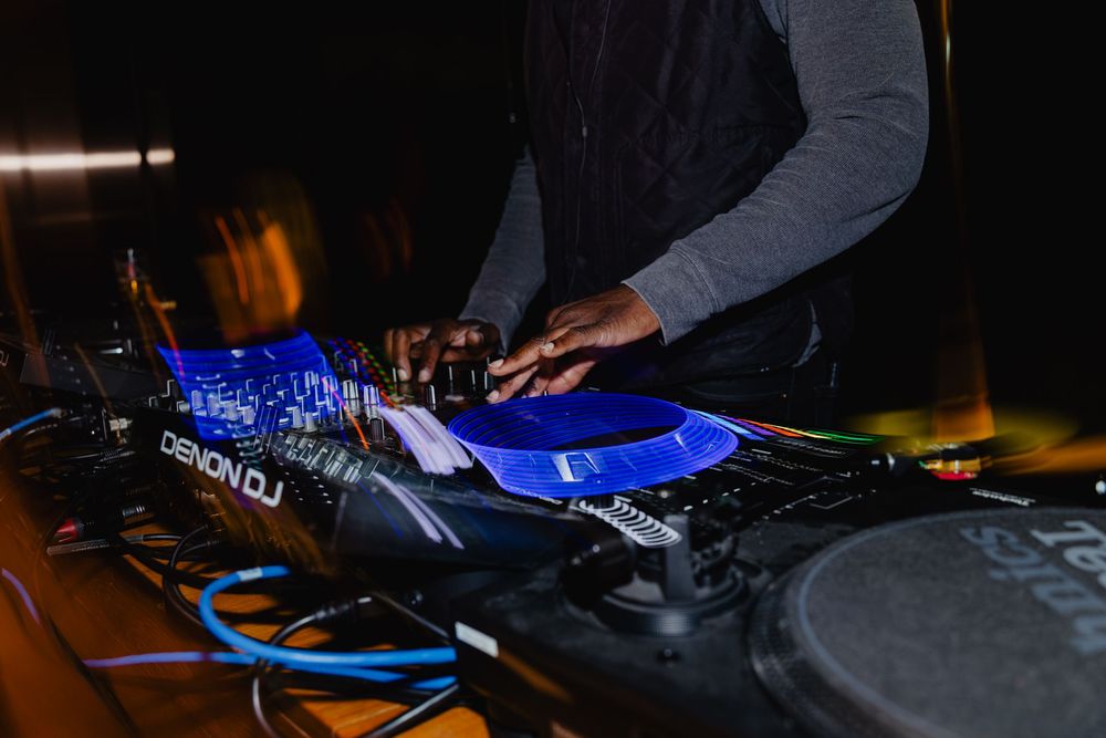 DJ performing at a nightclub with turntables and mixing equipment illuminated by blue and orange lighting.