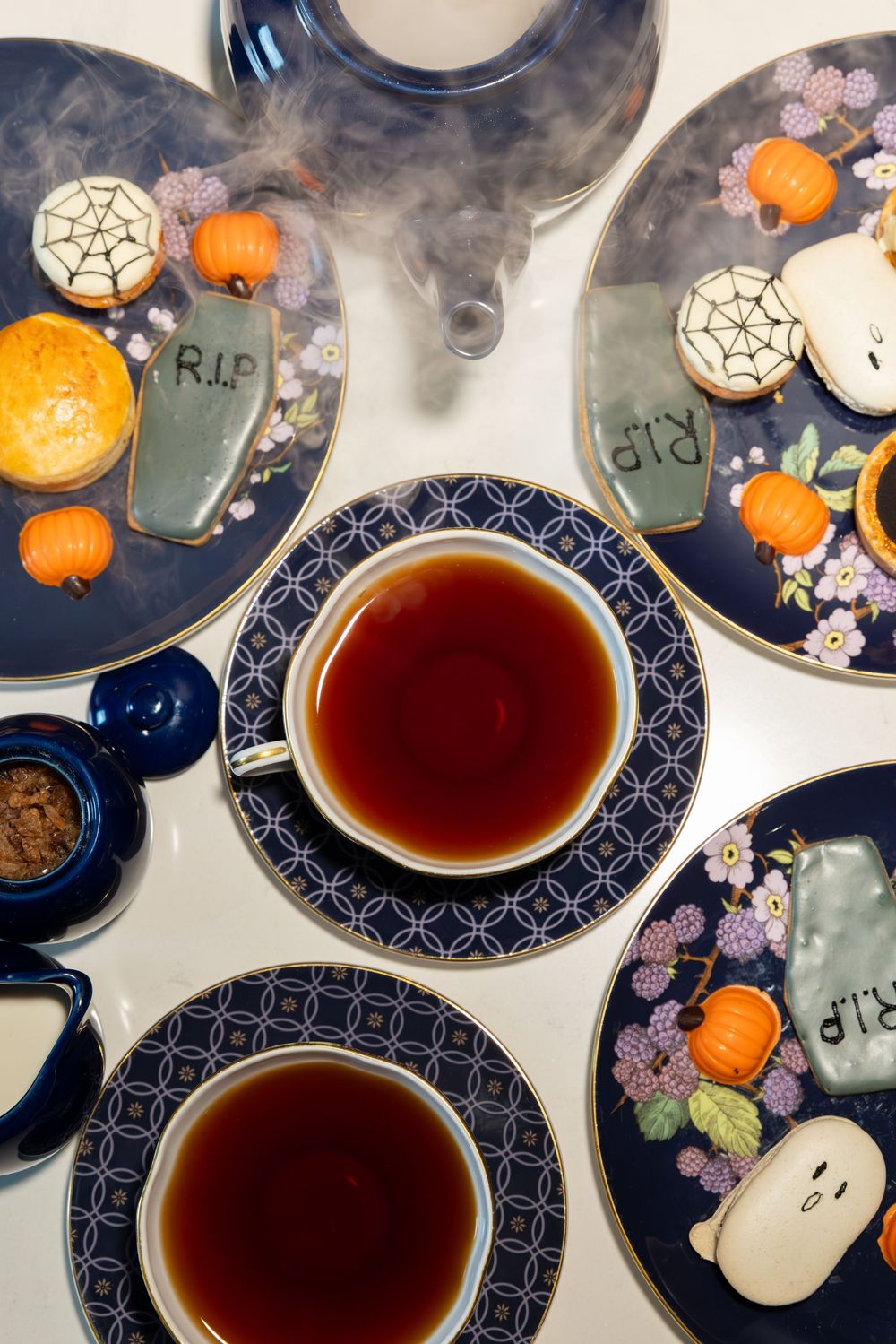 A Halloween-themed tea party setting with dark blue plates, small pumpkins, and spooky decorations in a misty atmosphere.