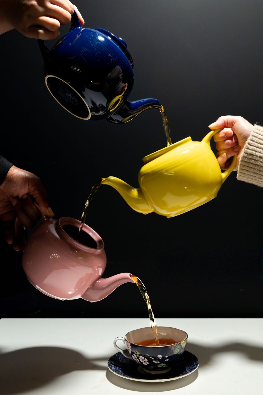 A sequence of coffee being poured from a blue kettle into a dark cup against a black background, creating artistic motion.