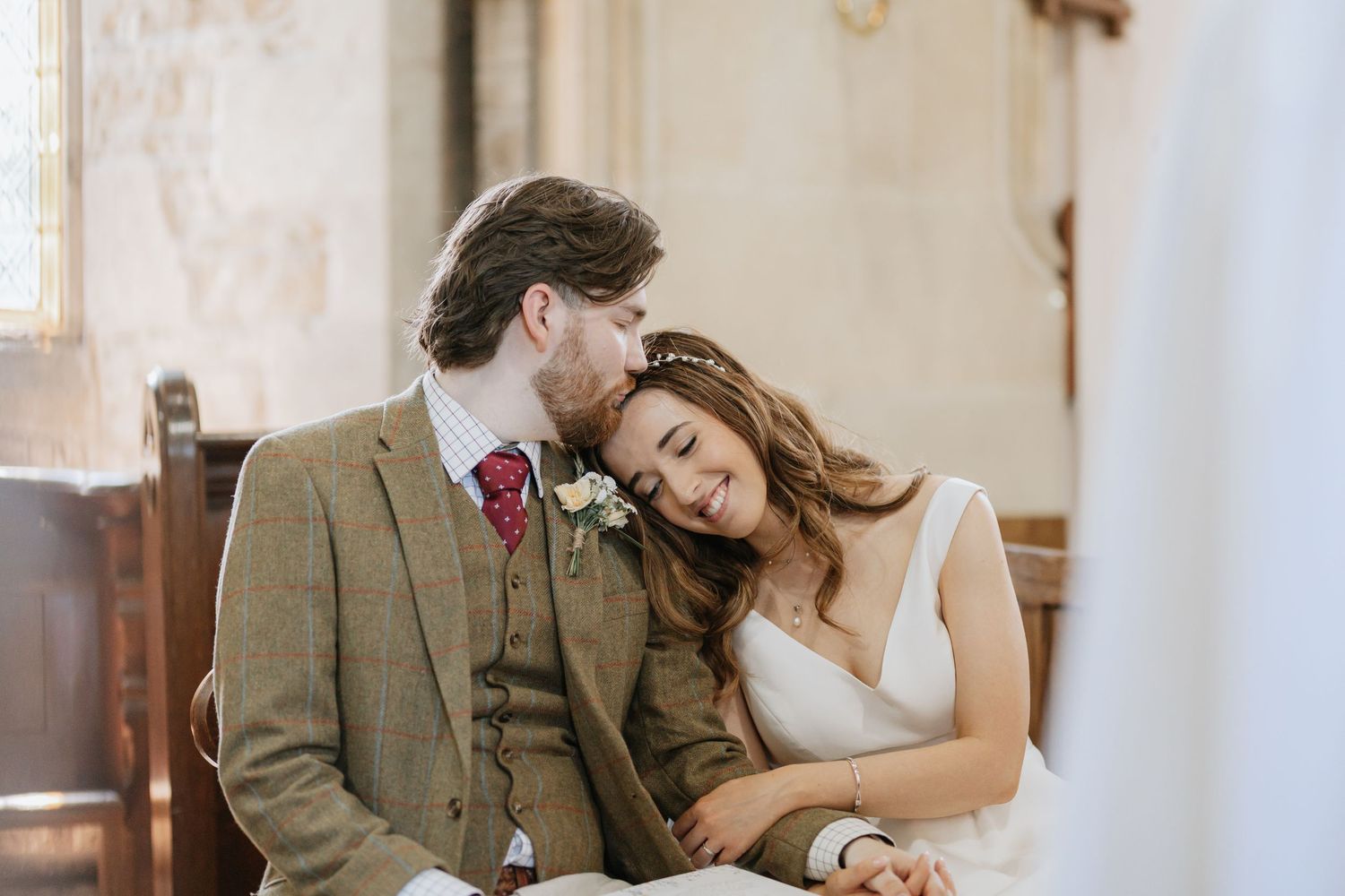 Romantic wedding couple embraces tenderly in a rustic setting with warm lighting.