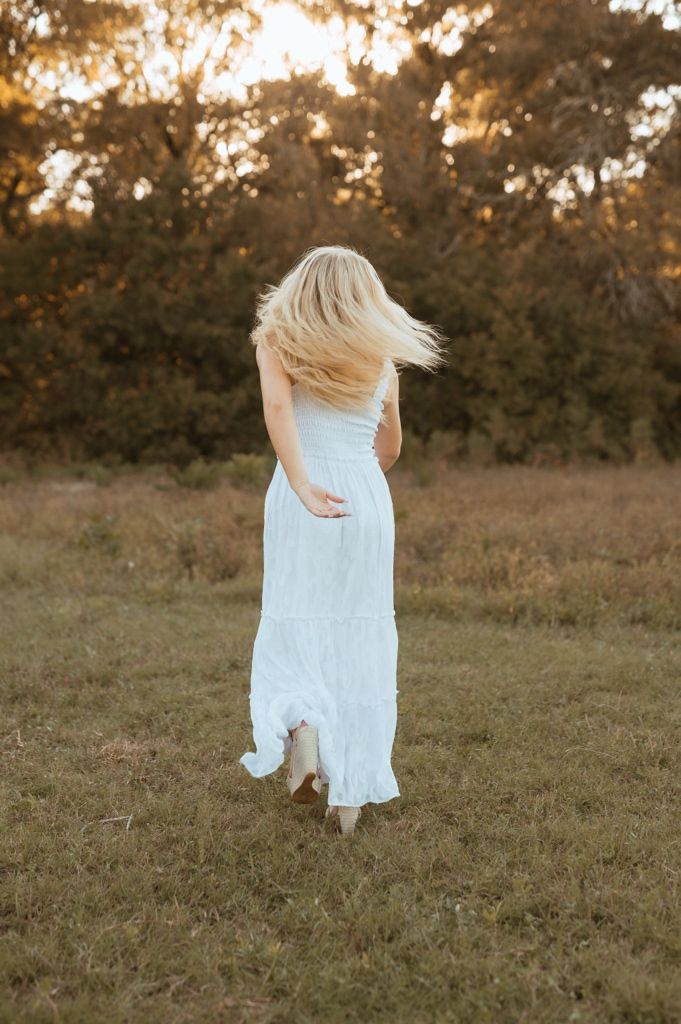 A person in a light blue dress twirls in a grassy field during golden hour sunset.