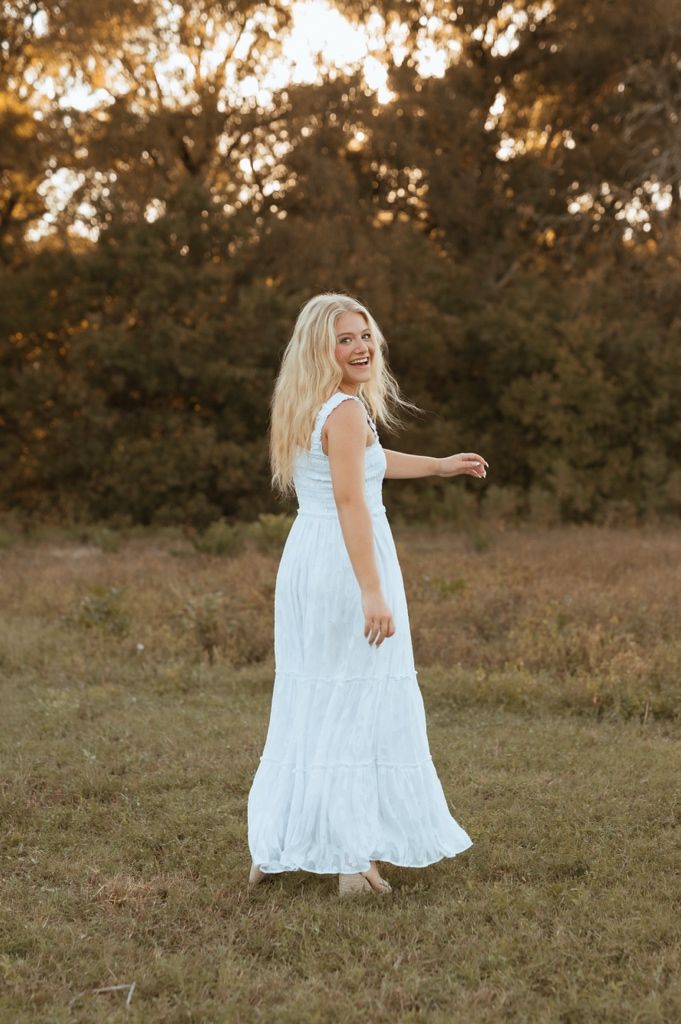 Dancing figure in a white summer dress spins joyfully in a sunlit field at dusk.