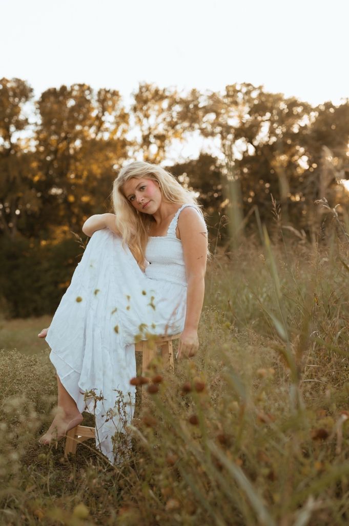 Woman in white dress twirls playfully in a golden sunlit field during sunset.