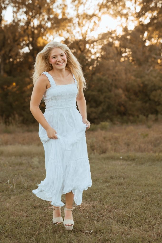 A person in a flowing white dress twirls joyfully in a sunlit field during golden hour.
