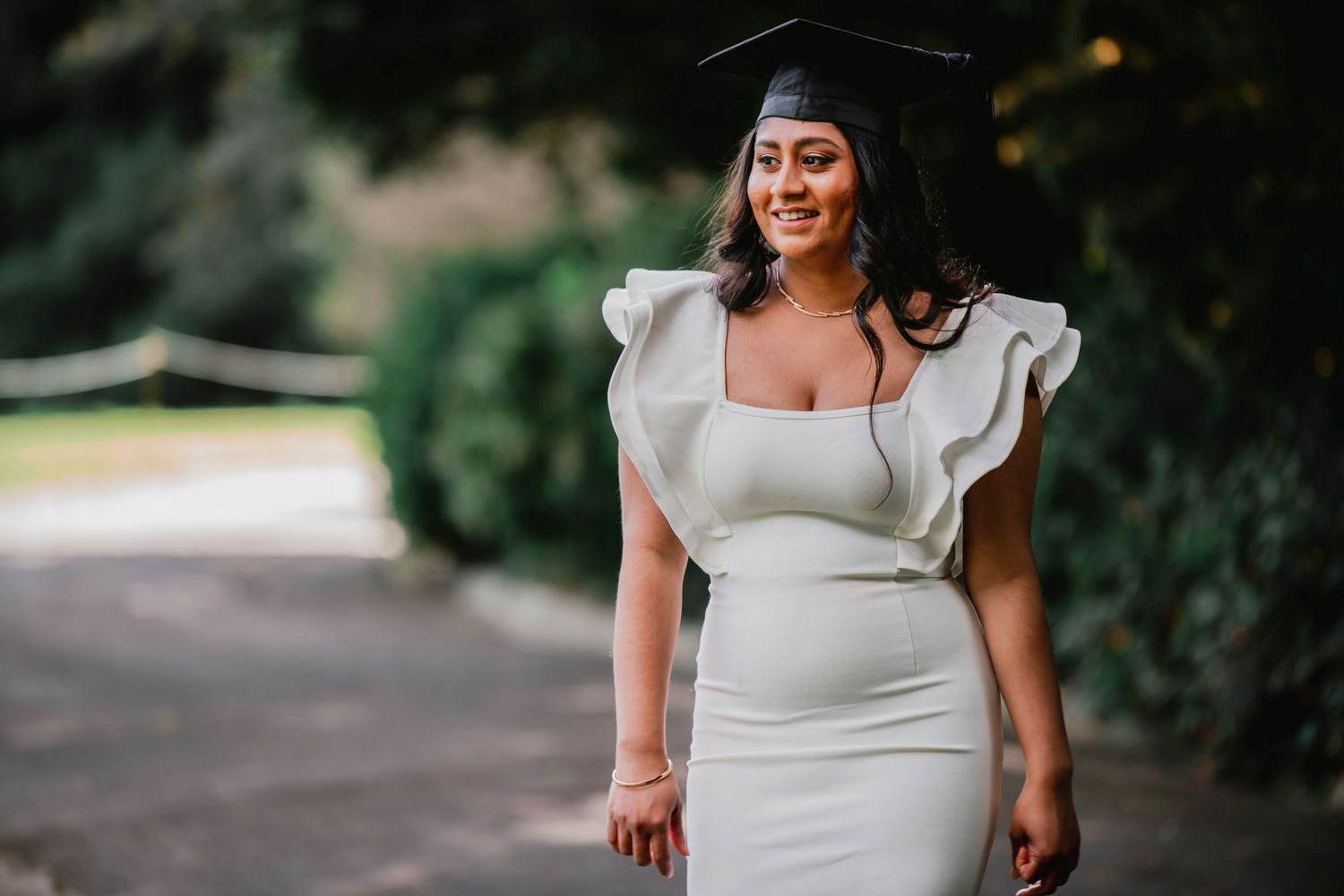 A bride in a white wedding dress with ruffled sleeves walks through a garden setting on a sunny day.