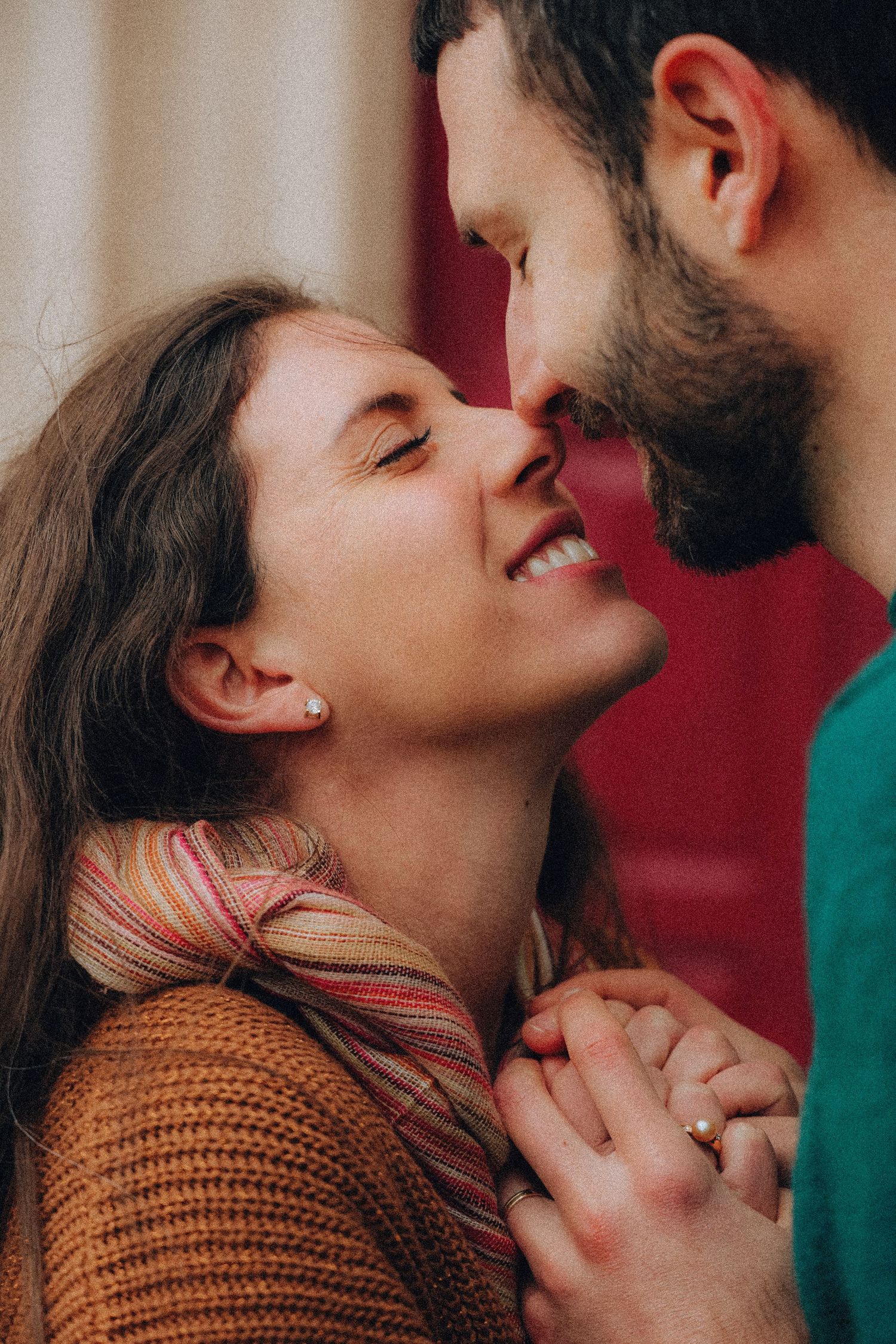 Romantic couple almost kissing indoors, smiling woman in orange knit sweater holding hands with bearded man.