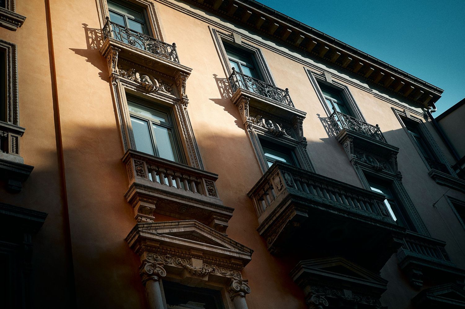 Historic Italian building facade with ornate balconies and architectural details against blue sky in Venice, Italy.