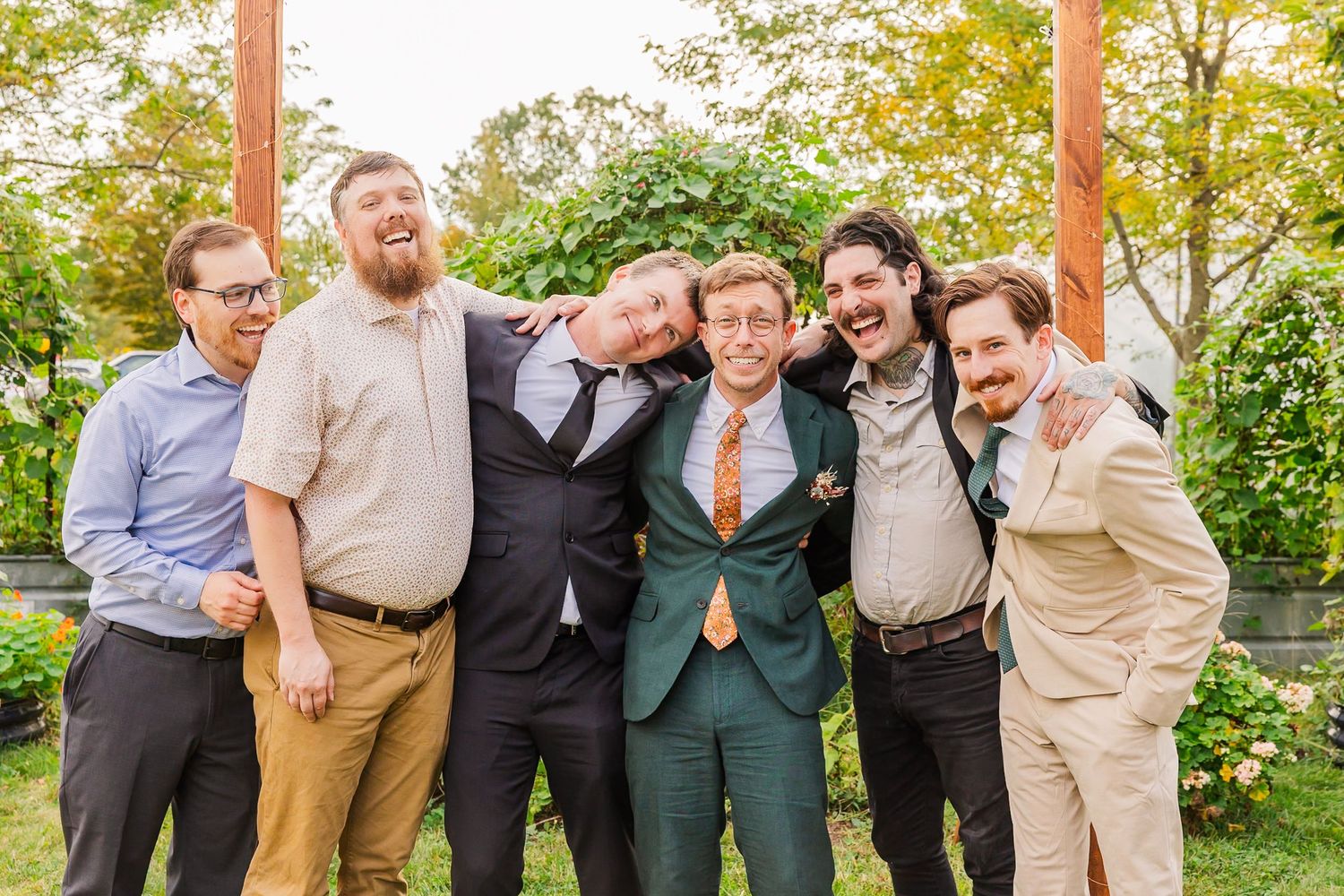 A group of groomsmen in suits pose playfully together outdoors for wedding party photos.