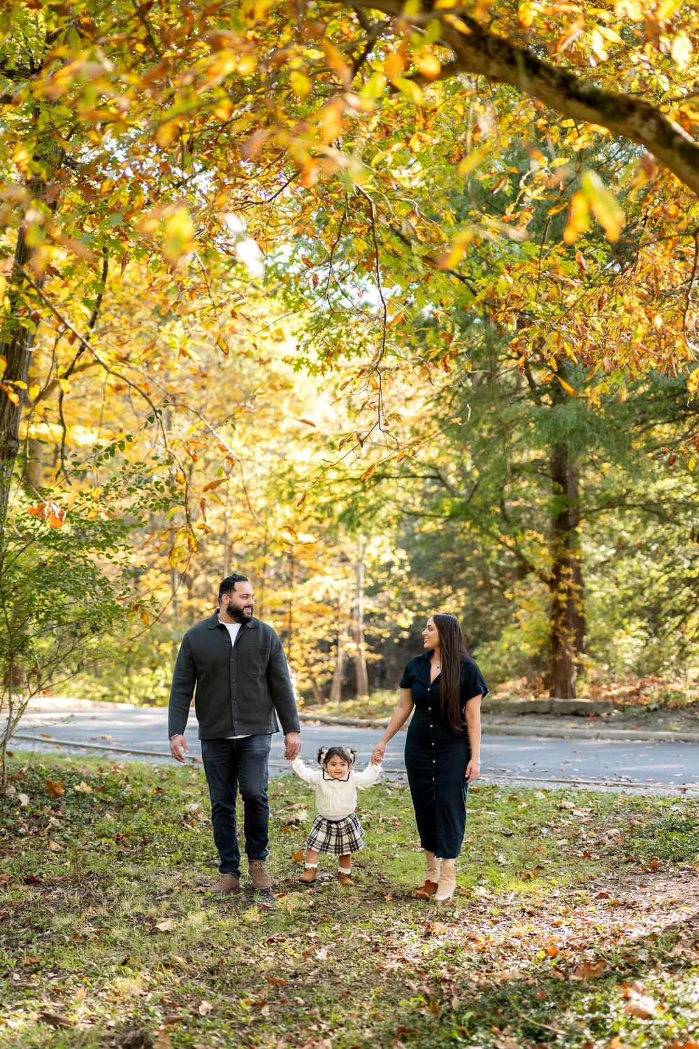 Happy family of three walking together under golden fall foliage in a sunny park.