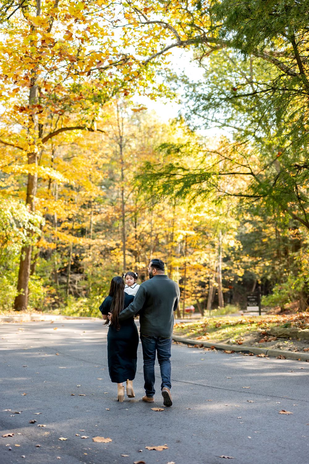 Couple walking hand-in-hand down tree-lined road surrounded by vibrant fall foliage.