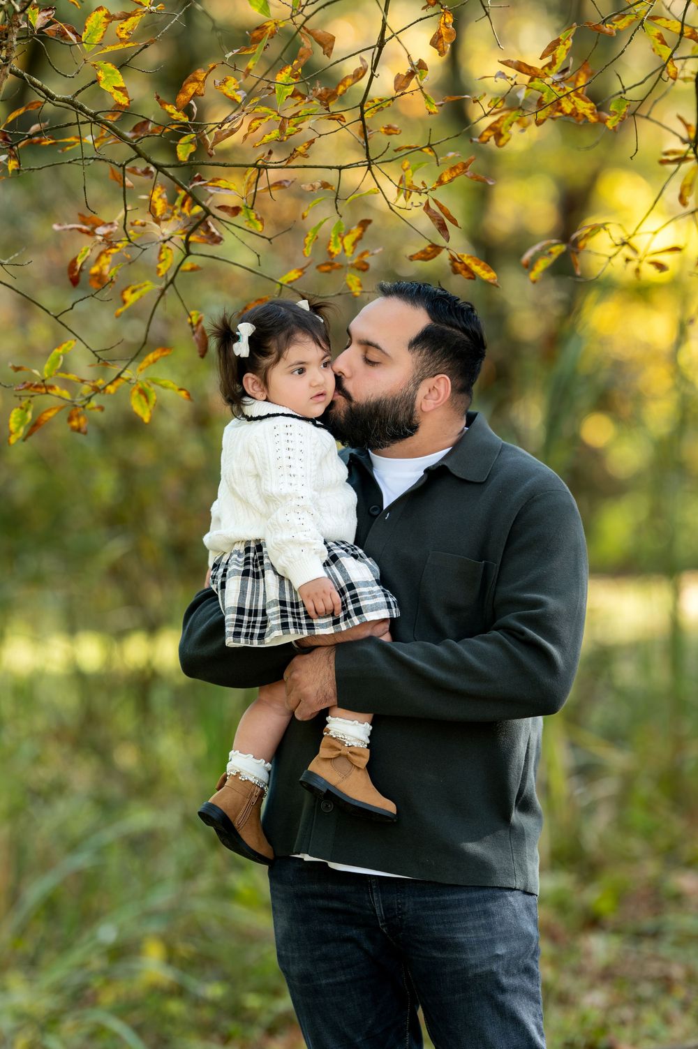 Loving father kissing toddler daughters cheek in golden autumn park setting.