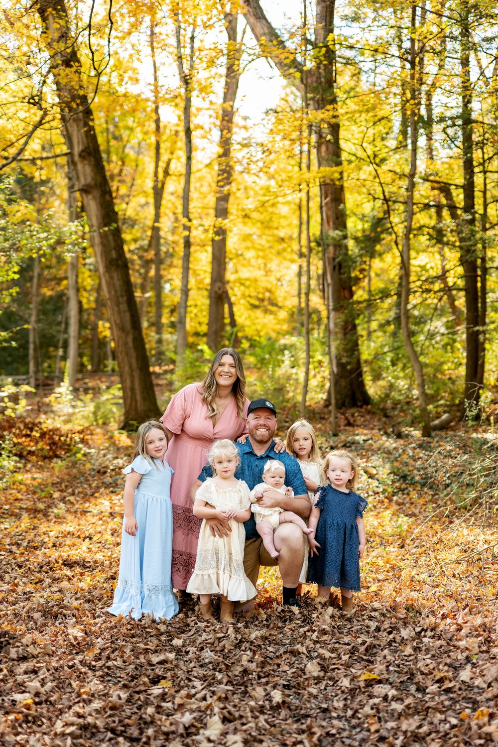 Family of six with four young daughters posing in vibrant yellow autumn woods.