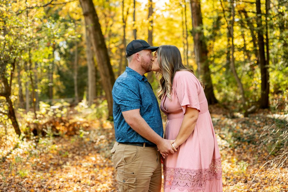 Romantic couple sharing a kiss surrounded by golden fall foliage in the woods.