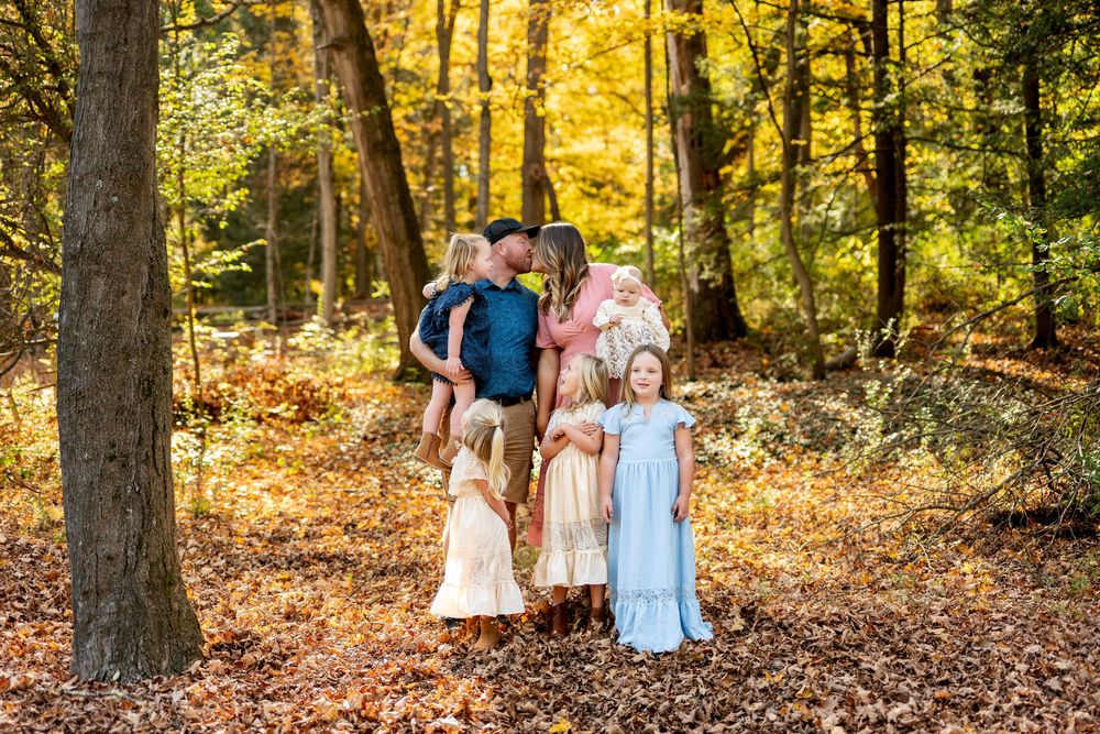 A playful family of seven shares a fun candid moment among colorful fall leaves in a forest.