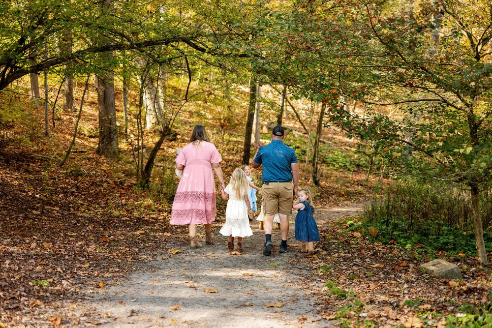 Family of five walking down an autumn forest path, with parents and children dressed in pink, blue, and white.