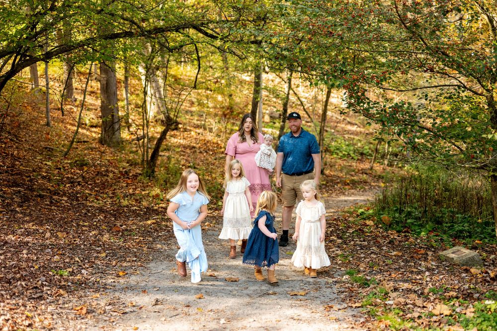 Family with four children walking on a wooded path surrounded by colorful fall foliage.