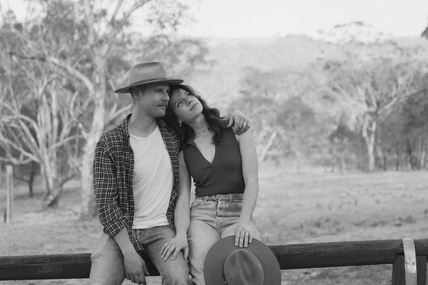 candid moment of couple sitting on a farm fence looking into the distance.