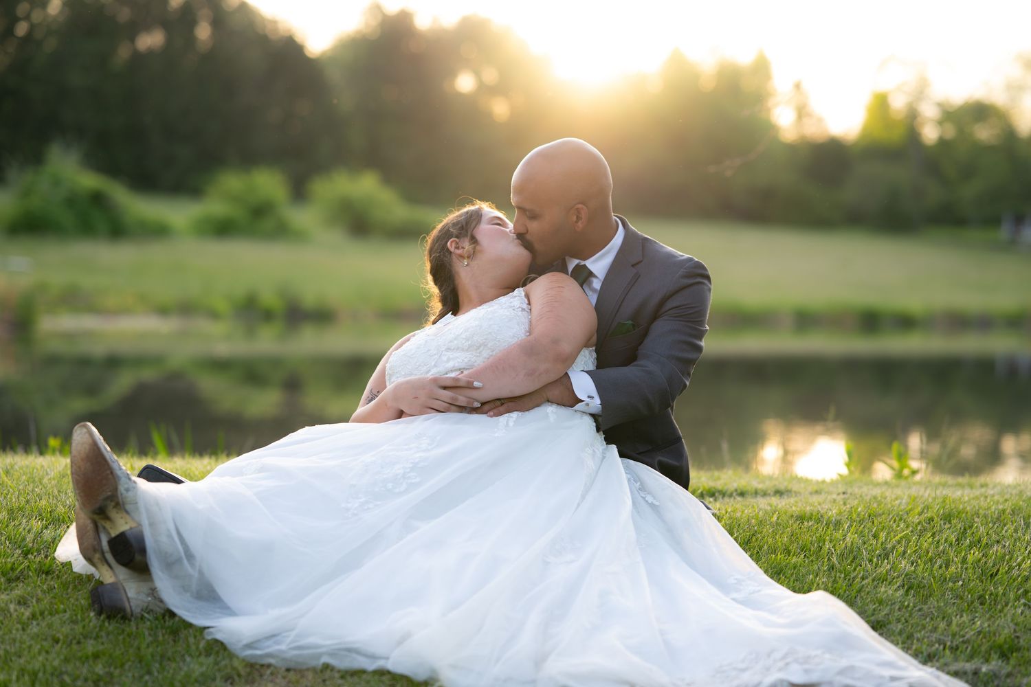 Wedding couple poses romantically on grass with dramatic sunset lighting.
