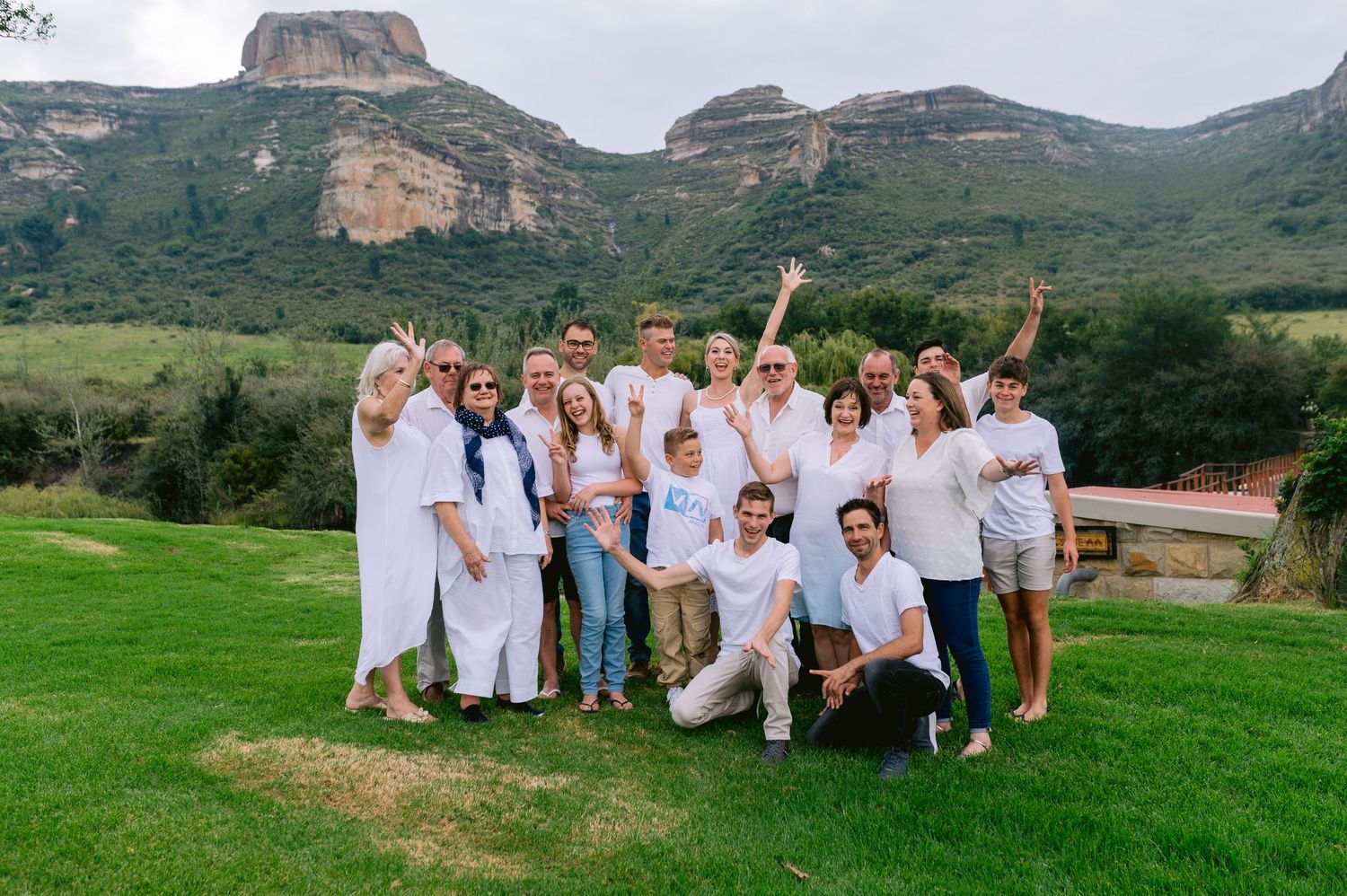 A group wearing white clothing poses together on a grassy hillside with mountains in the background.