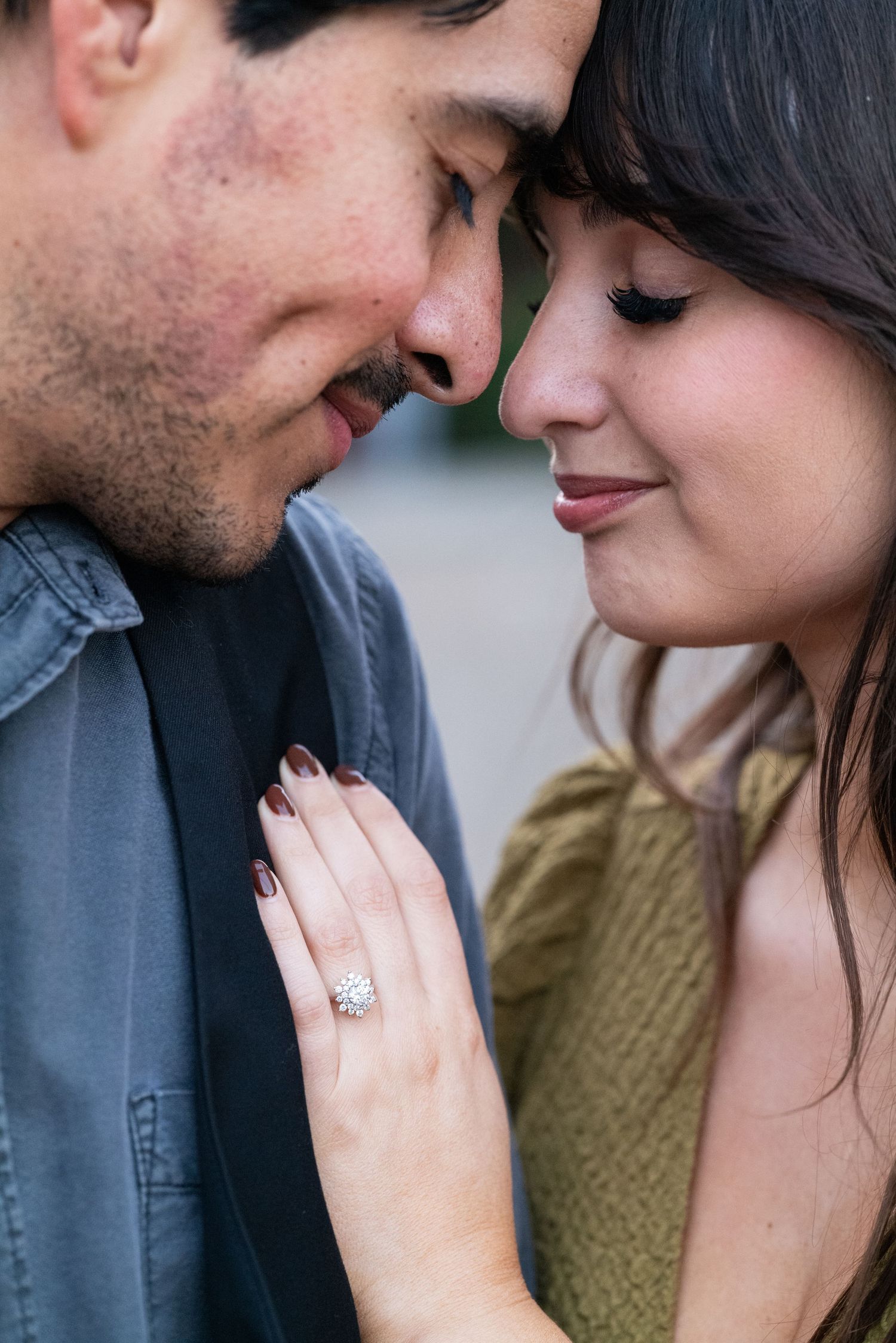 Close-up of newly engaged couple touching foreheads tenderly while woman displays her diamond ring.