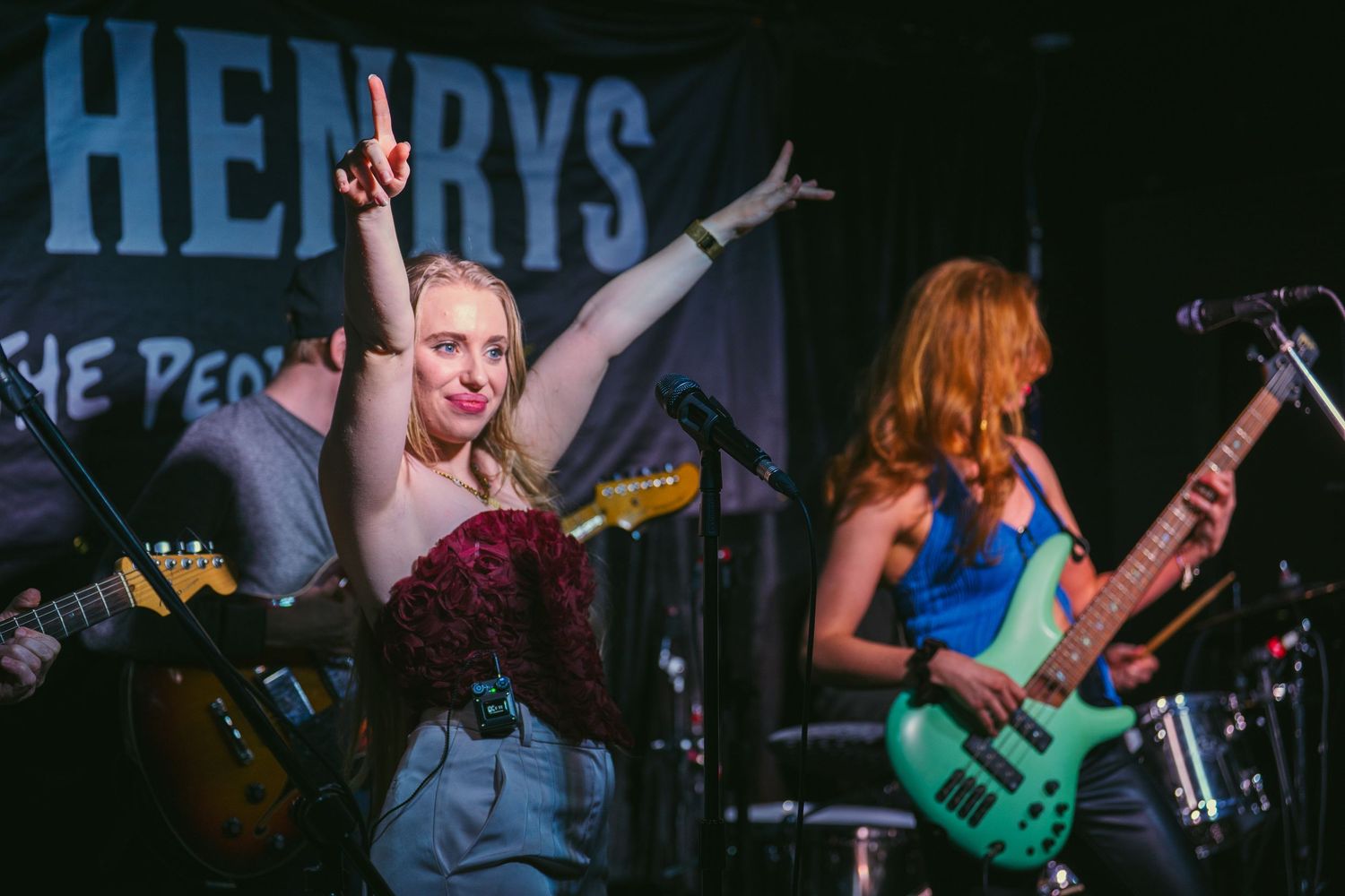 Female vocalist raises hand on stage at Henrys venue with bassist performing behind her.