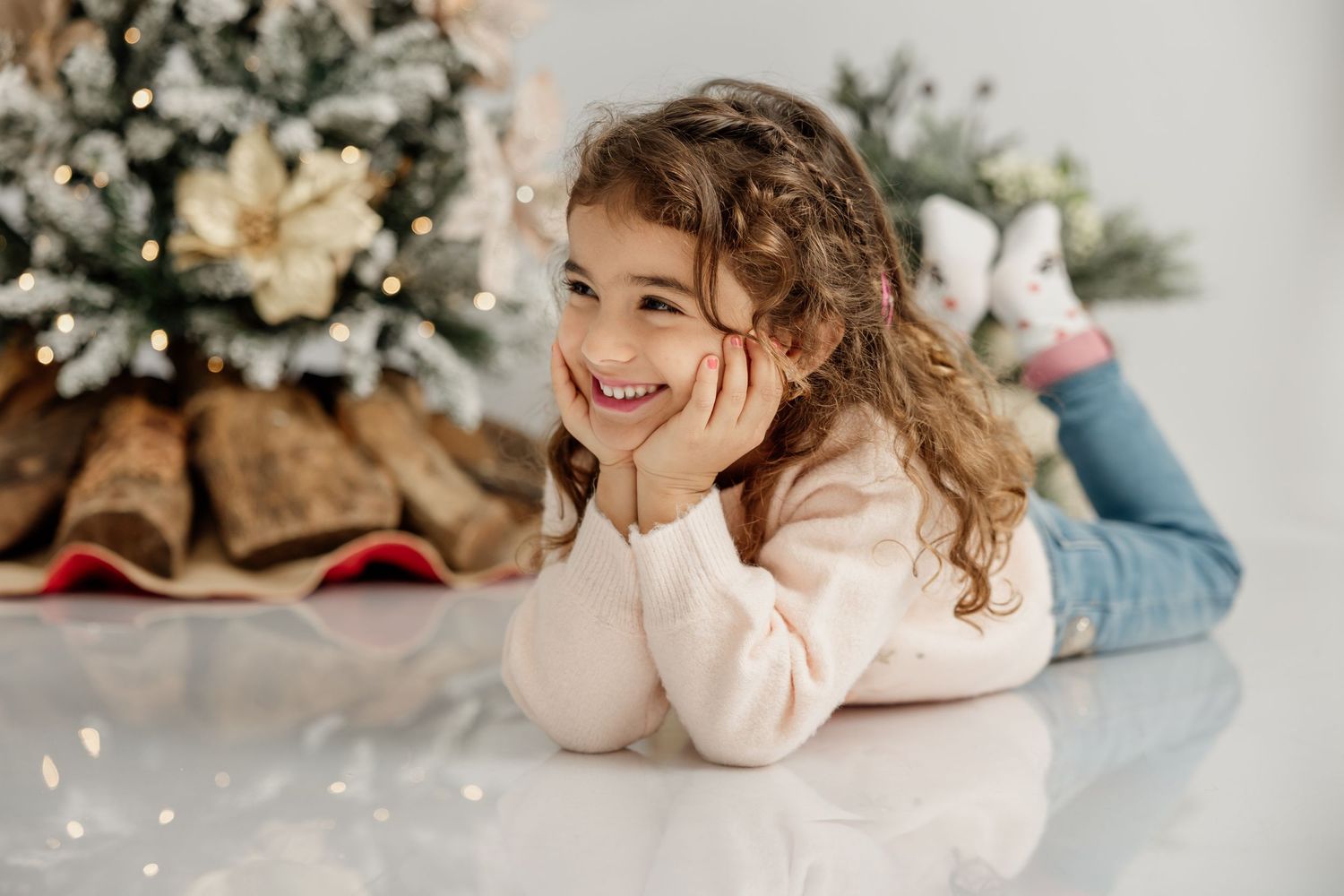 A young child in a green striped sweater playfully poses on a rustic wooden bench with holiday decorations in background.