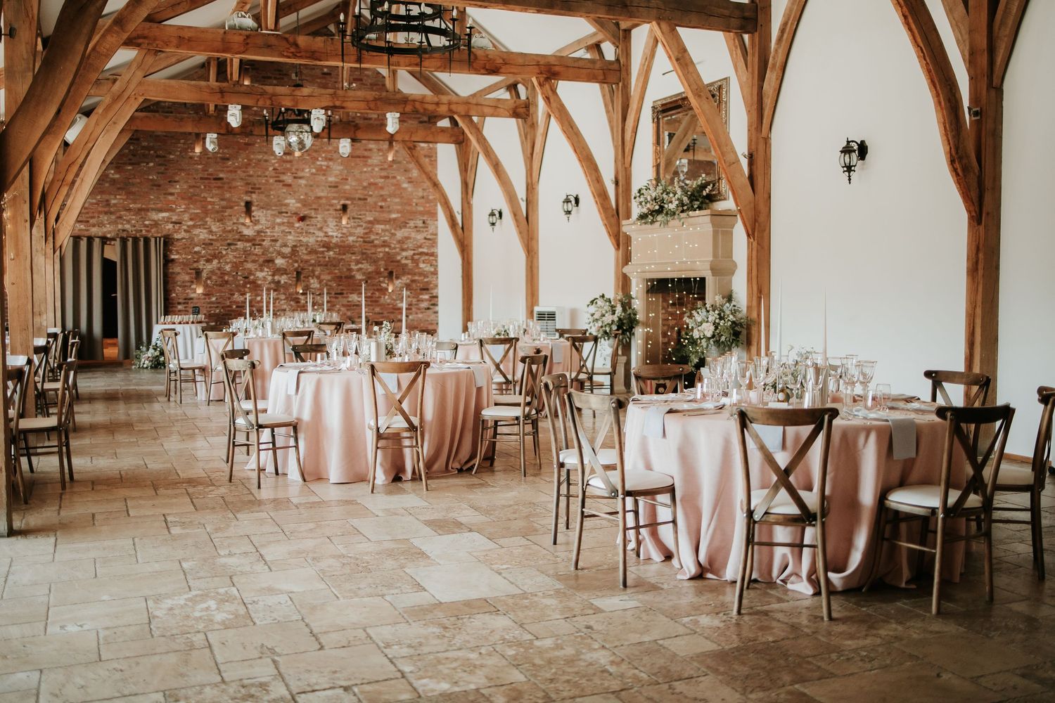 Rustic barn wedding venue interior with exposed wooden beams and elegant table settings in warm natural light.