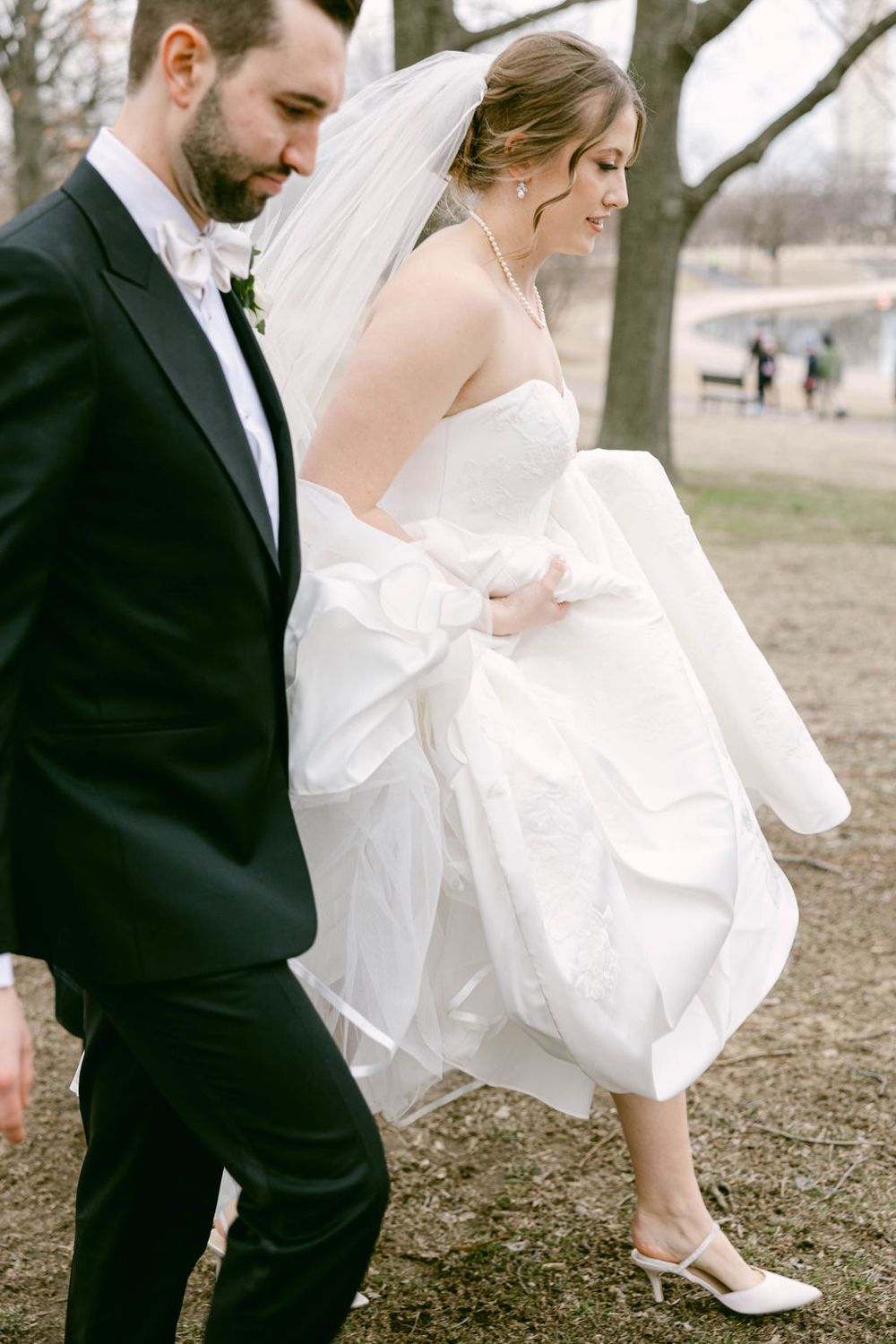 Elegant wedding couple walking outdoors with bride's white dress flowing in the breeze.