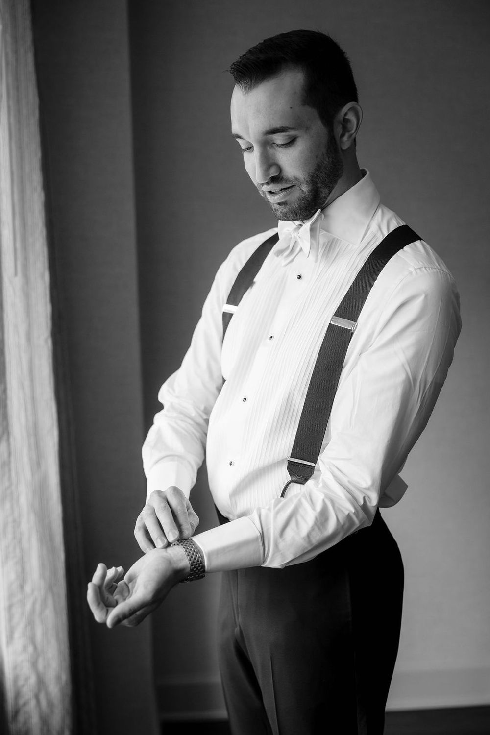Black and white series of a groom getting ready, adjusting his suspenders in formal attire.