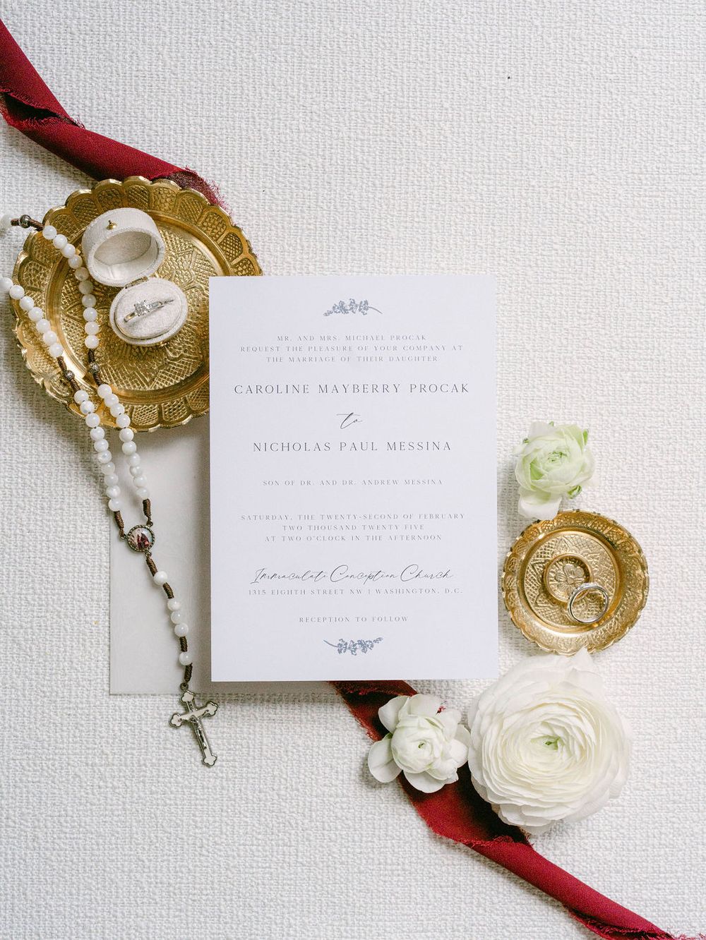 Elegant wedding invitation suite with white flowers and gold accents on a textured background.