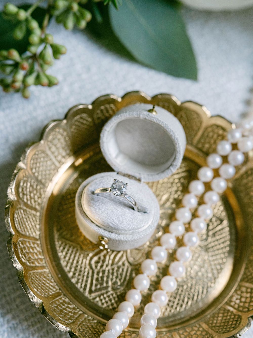A gold vintage plate with ornate patterns and a pearl necklace draped elegantly across its decorative surface.