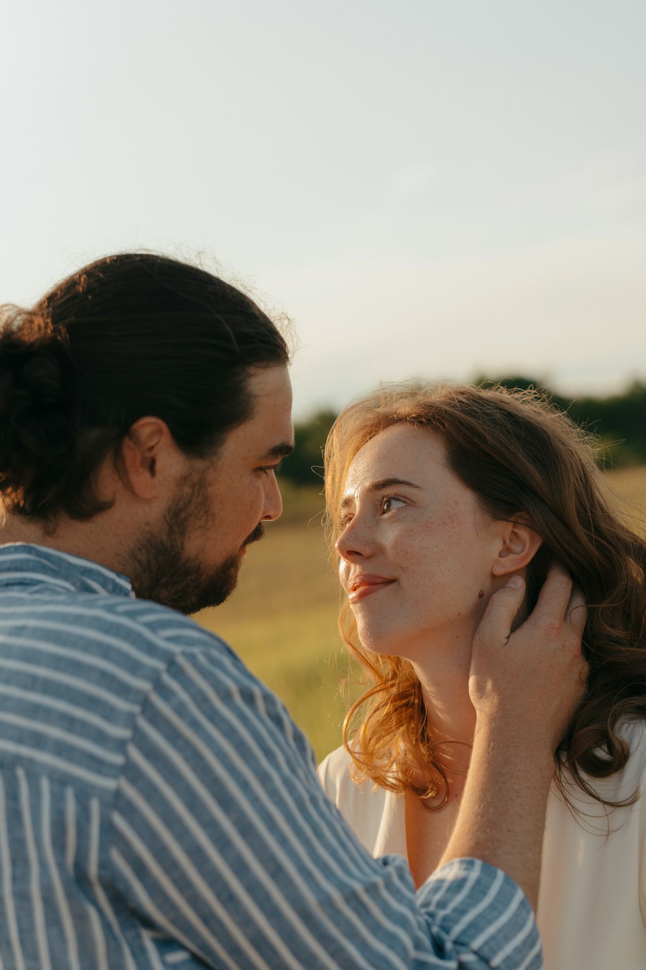 A romantic couple shares an intimate moment in a sunlit field during golden hour.