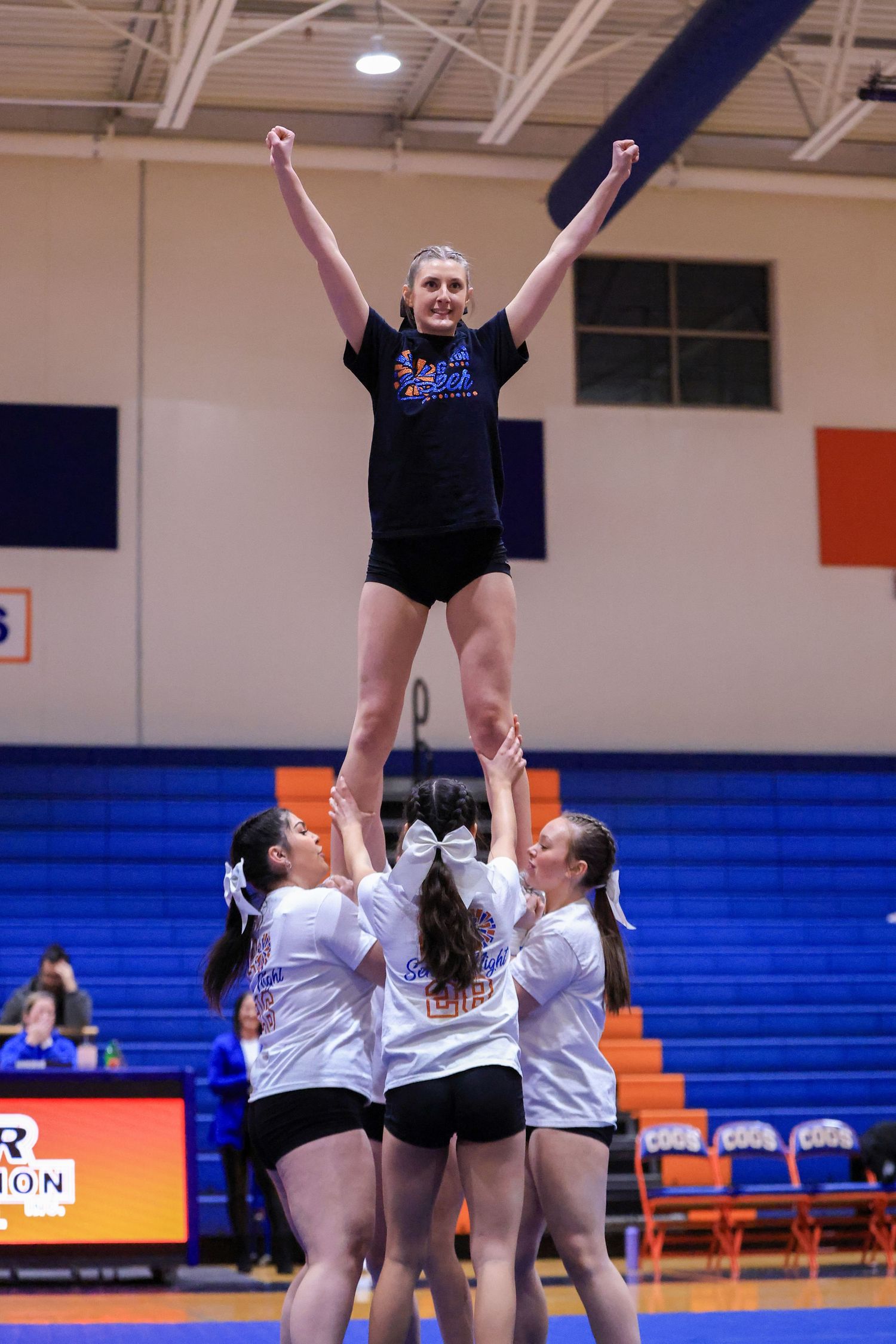 Cheerleaders executing stunt formation in indoor gymnasium.
