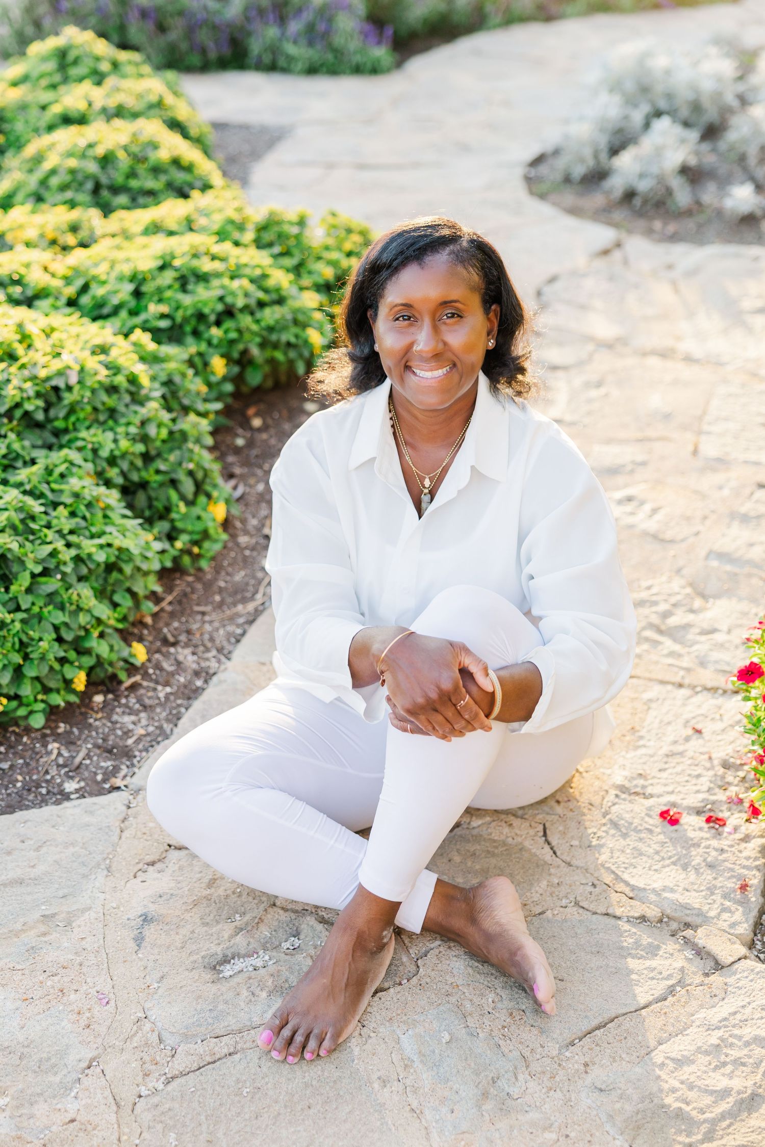 A person wearing all white sits casually on stone pavers surrounded by lush greenery in an outdoor setting at Maymont Park in Richmond, VA