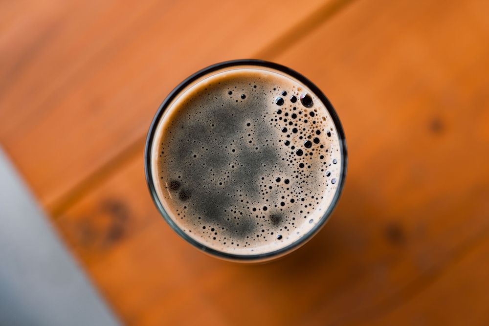 Overhead view of dark beer with foam bubbles in glass.
