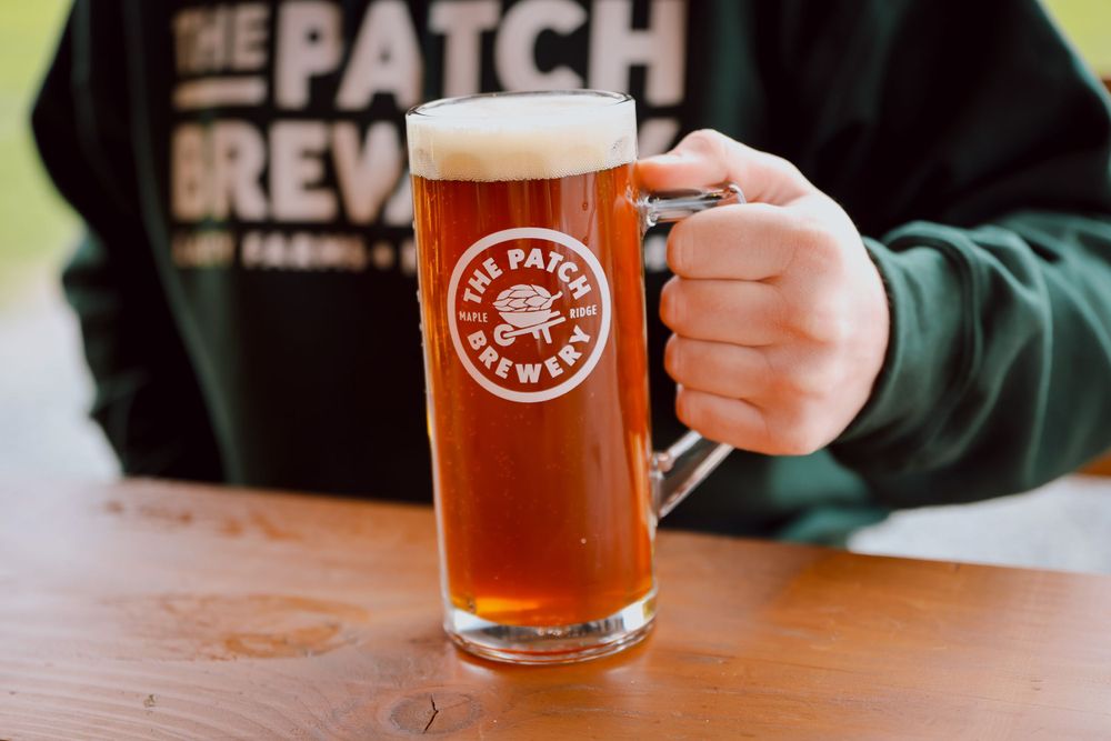 Person holding pint glass of amber beer with The Patch Brewery logo.