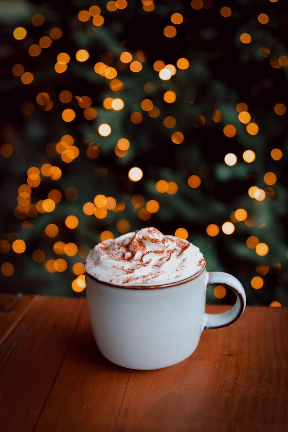 Hot chocolate with whipped cream against blurred holiday lights.