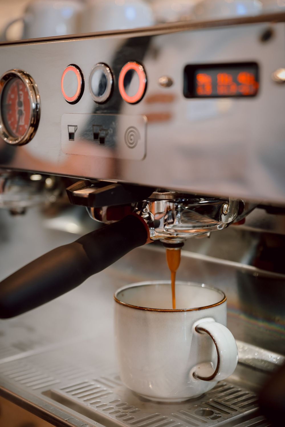 Espresso machine brewing fresh coffee into white ceramic cup with precise temperature control.