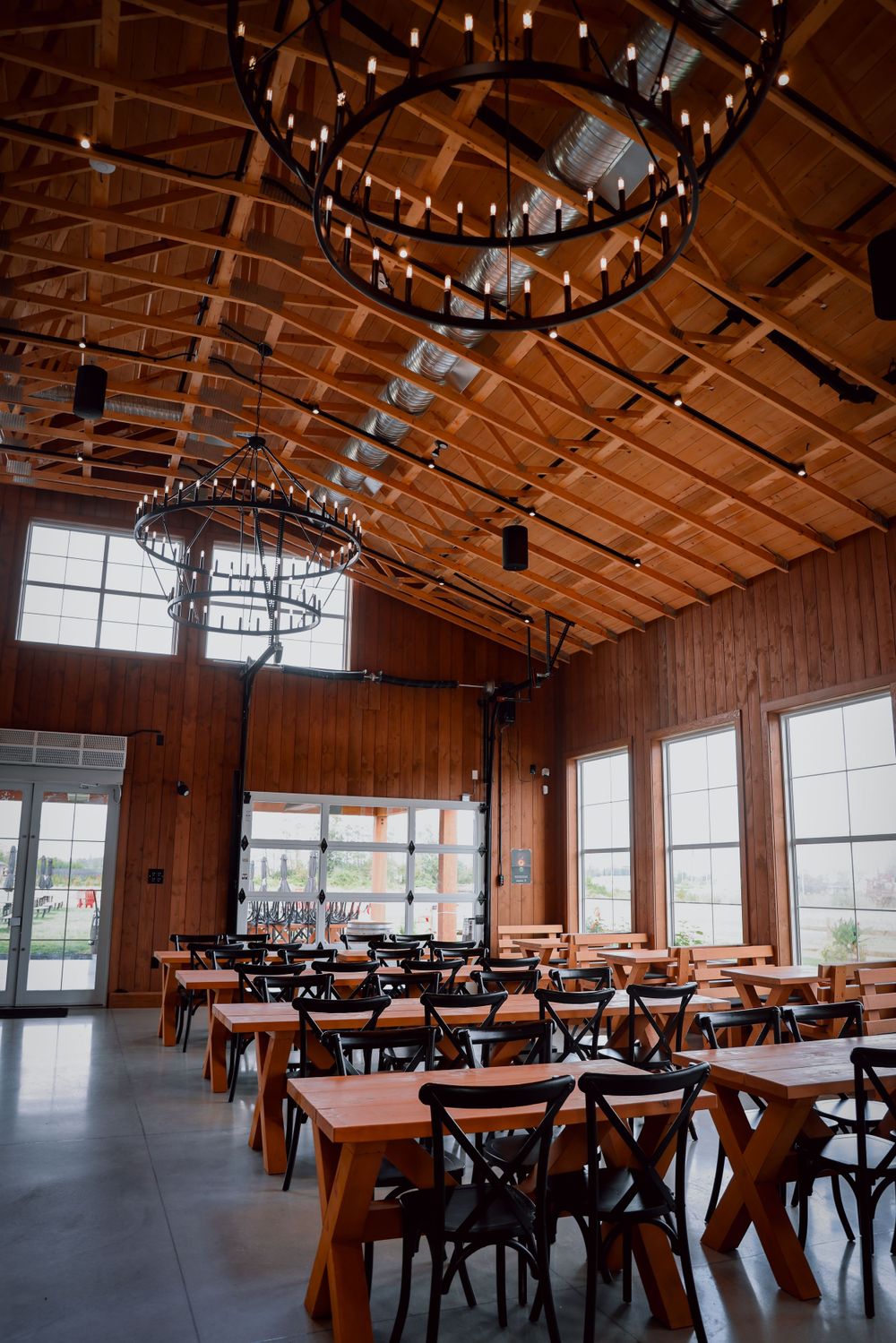 Restaurant dining room with vaulted wooden ceiling, circular chandeliers and rustic wooden tables.