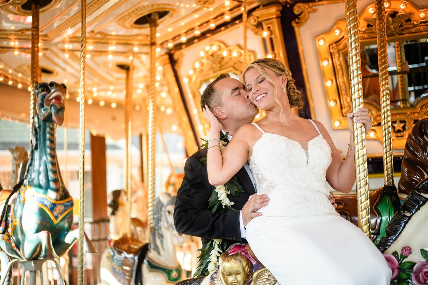 A romantic couple shares a tender moment while riding on an ornate carousel with glowing lights and decorative horses.