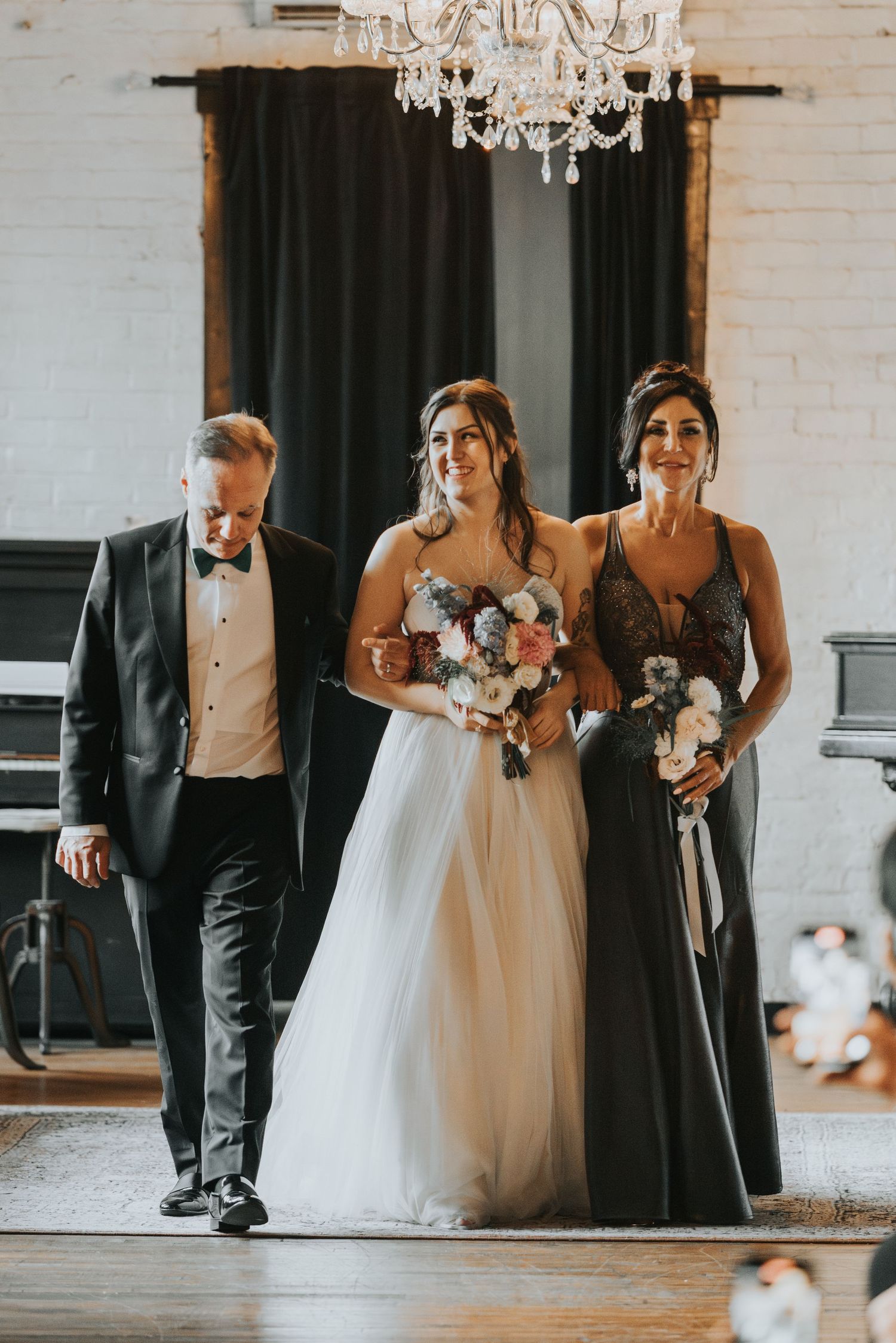 An elegant procession during a wedding ceremony features attendees in formal attire walking under a crystal chandelier.