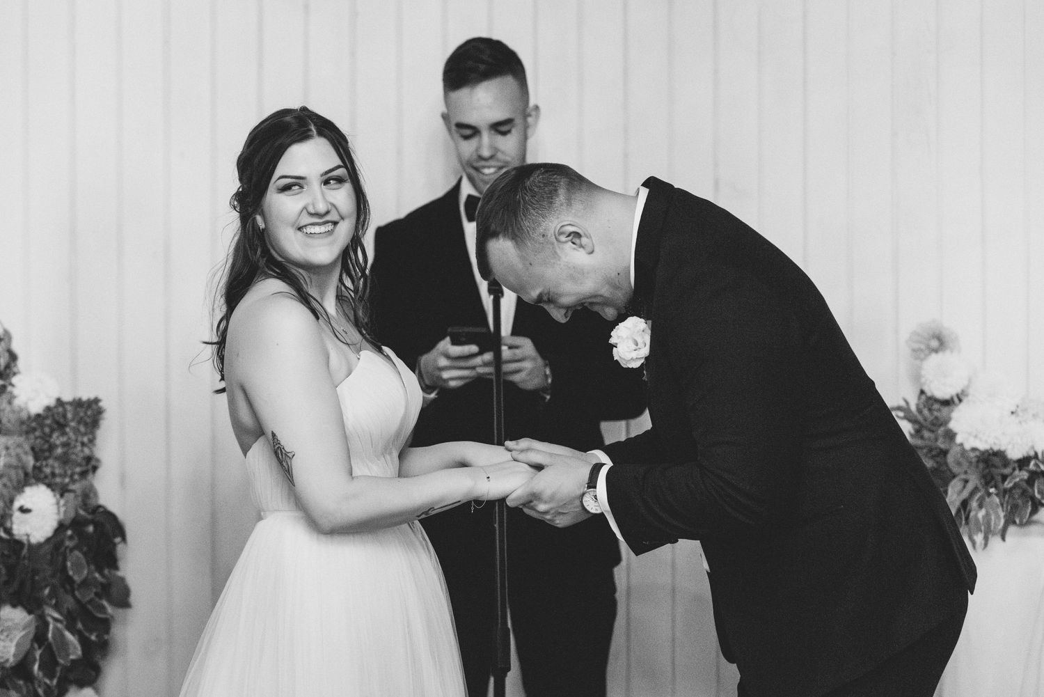 A joyful moment captured in black and white at a wedding ceremony between a couple in front of a curtain backdrop.