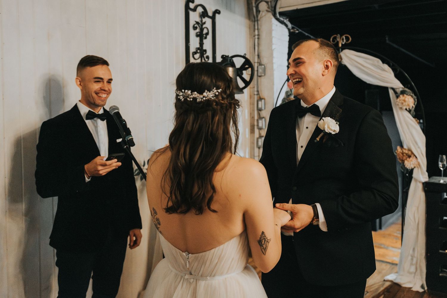 Two people share a joyful moment during a wedding ceremony under an ornate arch.
