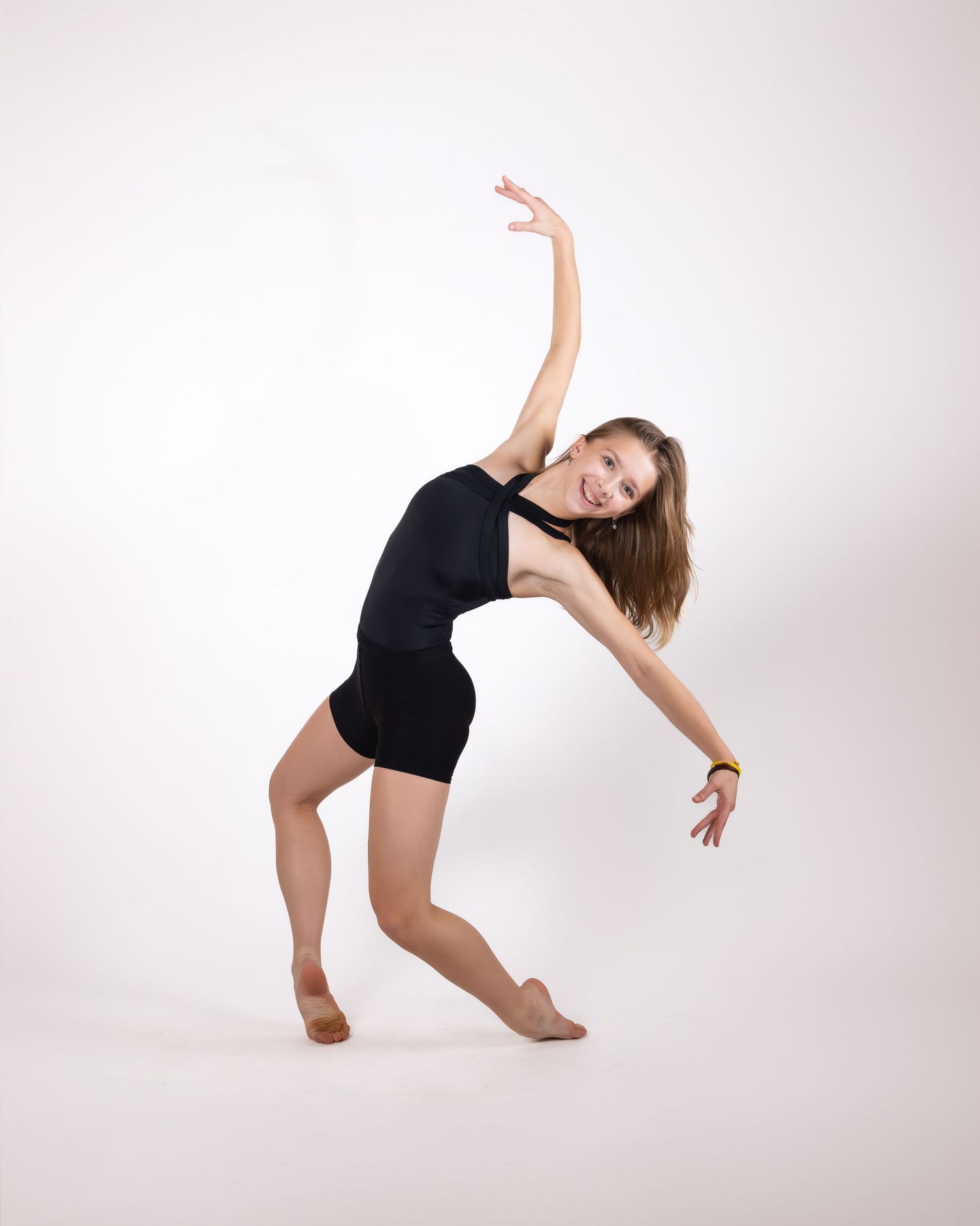 A dancer in a black leotard performs a graceful contemporary dance pose against a white studio backdrop.